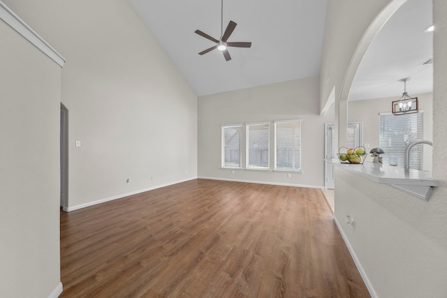 unfurnished living room with high vaulted ceiling, a wealth of natural light, baseboards, and wood finished floors