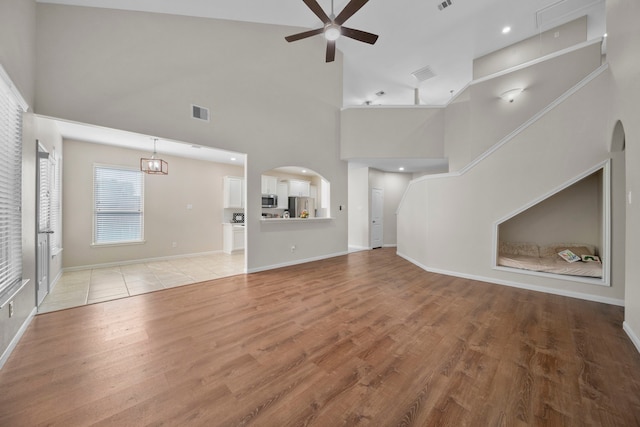 unfurnished living room with light wood finished floors, ceiling fan, arched walkways, and baseboards