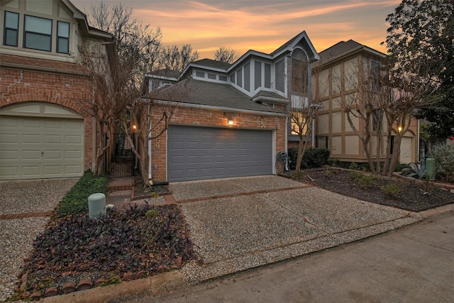 tudor-style house with concrete driveway, brick siding, an attached garage, and roof with shingles