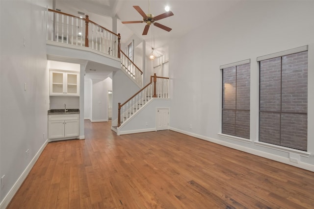 unfurnished living room featuring baseboards, wood-type flooring, stairs, a high ceiling, and a sink