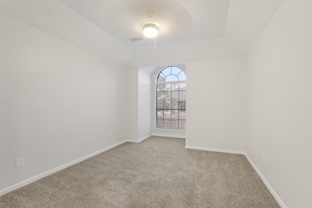 carpeted empty room with a tray ceiling, visible vents, and baseboards