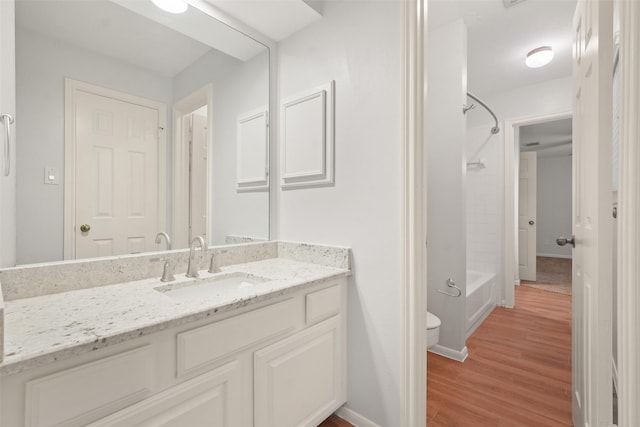 bathroom featuring baseboards, toilet, vanity, wood finished floors, and shower / bathtub combination