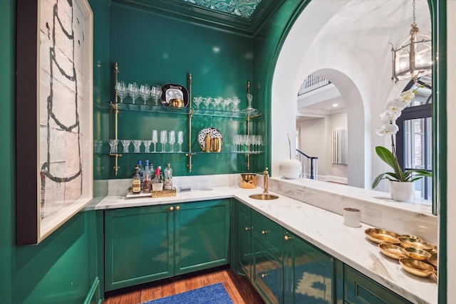 bar featuring arched walkways, indoor wet bar, crown molding, a sink, and wood finished floors