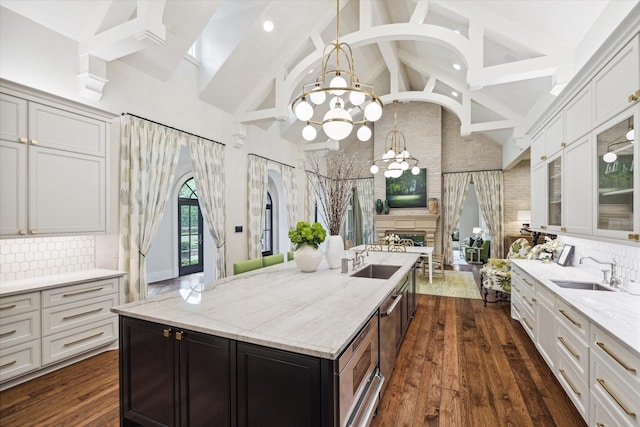 kitchen featuring dark wood-style flooring, a sink, backsplash, a center island with sink, and an inviting chandelier