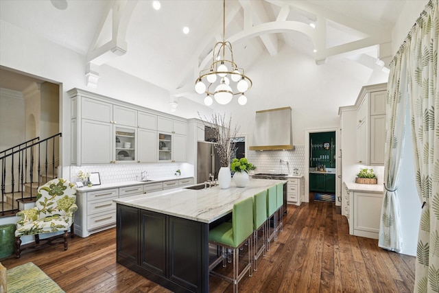 kitchen featuring a center island with sink, dark wood finished floors, wall chimney exhaust hood, a sink, and backsplash