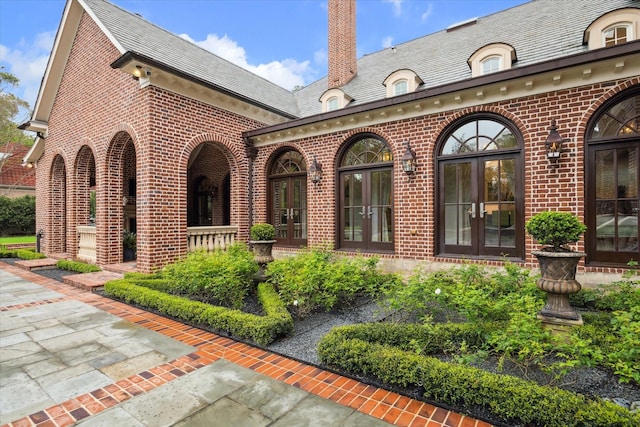 doorway to property featuring a high end roof, french doors, brick siding, and a chimney