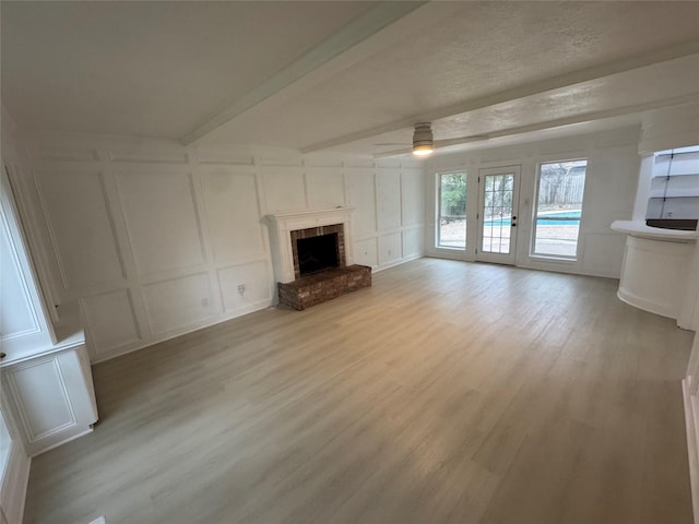 unfurnished living room with light wood-type flooring, a brick fireplace, a decorative wall, and beam ceiling