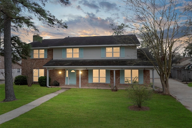 view of front of property featuring driveway, a chimney, a front lawn, and brick siding