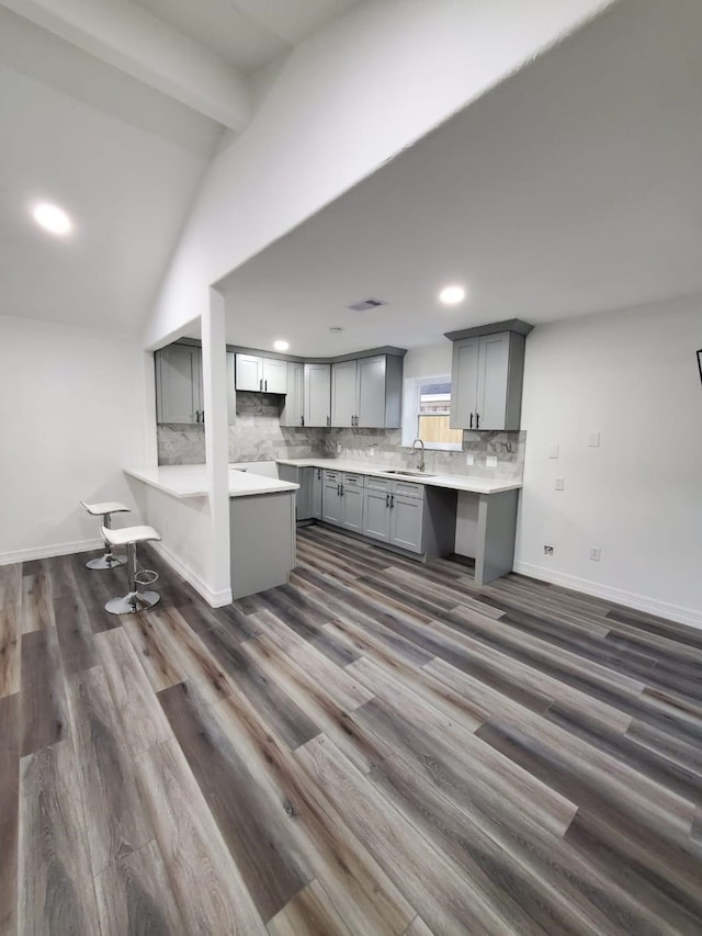 kitchen featuring vaulted ceiling with beams, tasteful backsplash, gray cabinets, a sink, and baseboards