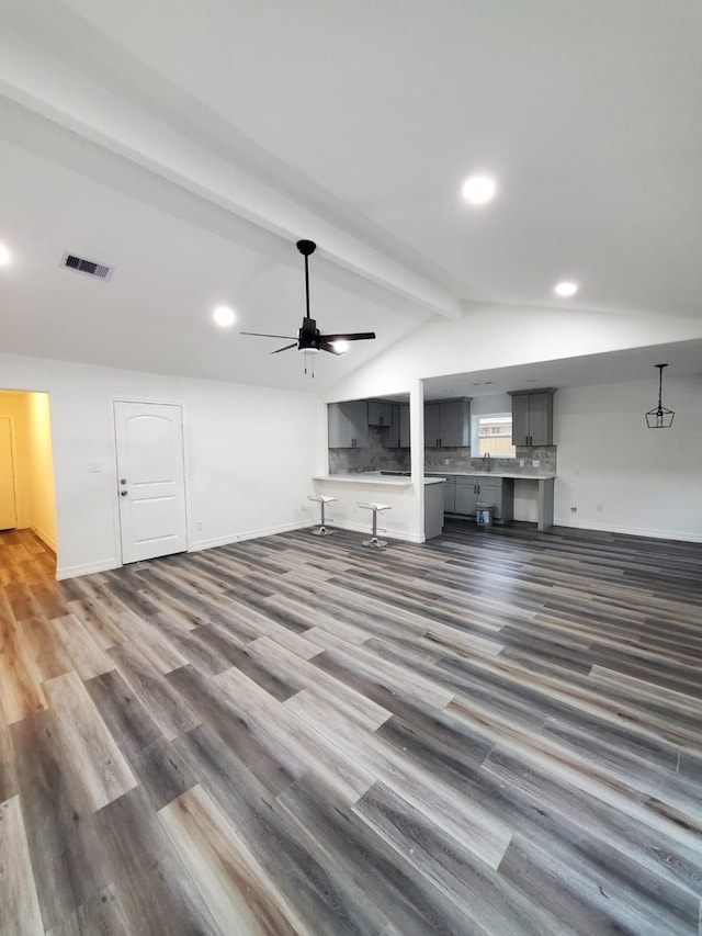 unfurnished living room featuring lofted ceiling with beams, wood finished floors, a ceiling fan, visible vents, and baseboards