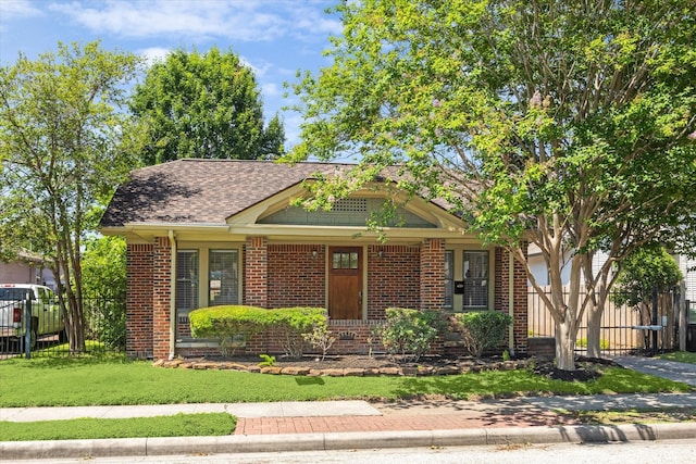 view of front of house featuring fence, roof with shingles, covered porch, a front yard, and brick siding