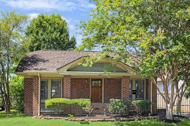 view of front facade featuring fence, brick siding, and roof with shingles