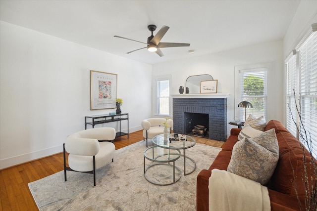 living area featuring baseboards, a brick fireplace, wood finished floors, and a ceiling fan