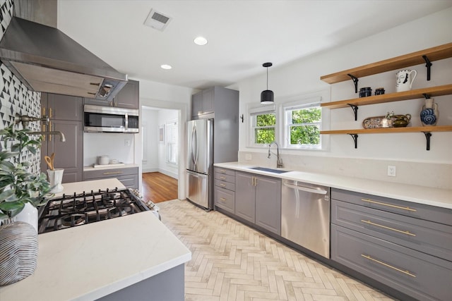 kitchen with visible vents, gray cabinets, a sink, stainless steel appliances, and wall chimney exhaust hood