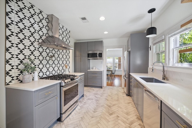 kitchen featuring wall chimney range hood, gray cabinets, appliances with stainless steel finishes, and a sink