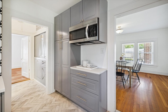 kitchen with stainless steel microwave, baseboards, light countertops, gray cabinets, and parquet floors