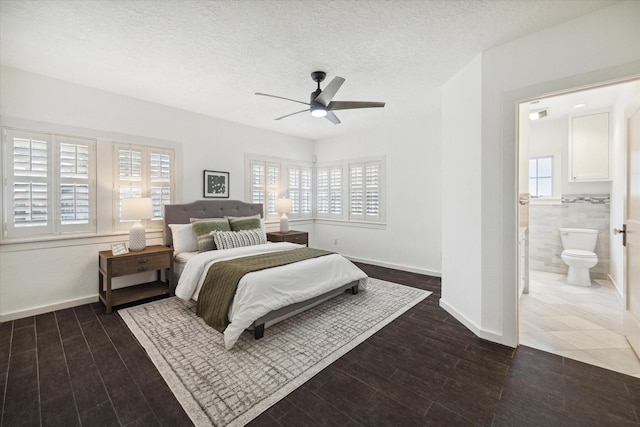 bedroom featuring dark wood-type flooring, ceiling fan, ensuite bathroom, a textured ceiling, and tile walls