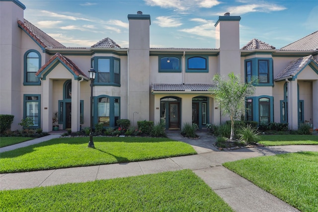 view of front of property with a front yard, a tile roof, a chimney, and stucco siding