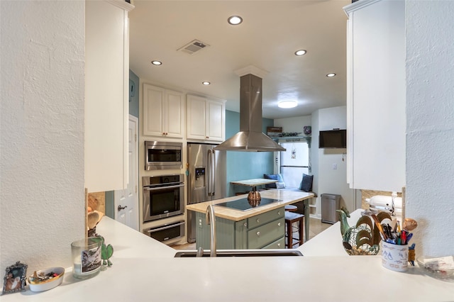 kitchen featuring visible vents, white cabinets, appliances with stainless steel finishes, island exhaust hood, and a sink