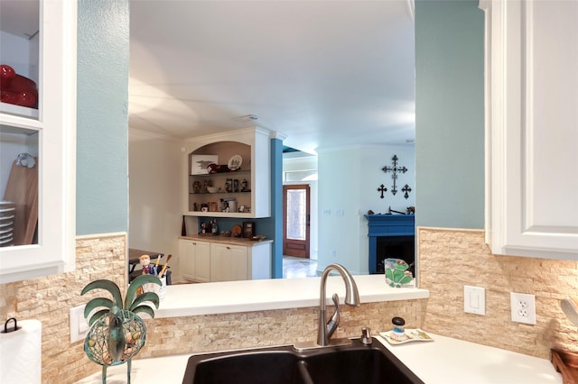 kitchen featuring a fireplace, a sink, white cabinetry, light countertops, and ornamental molding