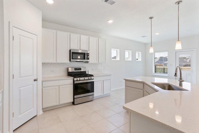 kitchen featuring decorative light fixtures, a sink, stainless steel appliances, white cabinetry, and backsplash