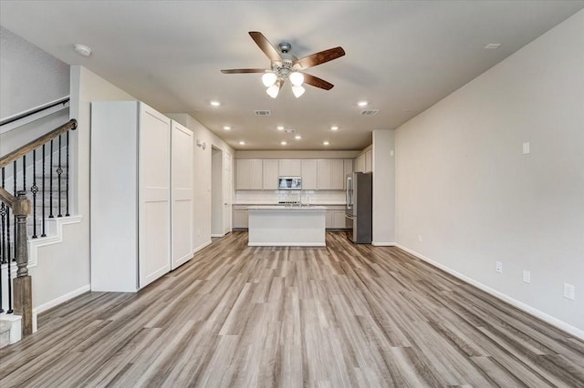 unfurnished living room featuring stairs, baseboards, light wood-style floors, and ceiling fan