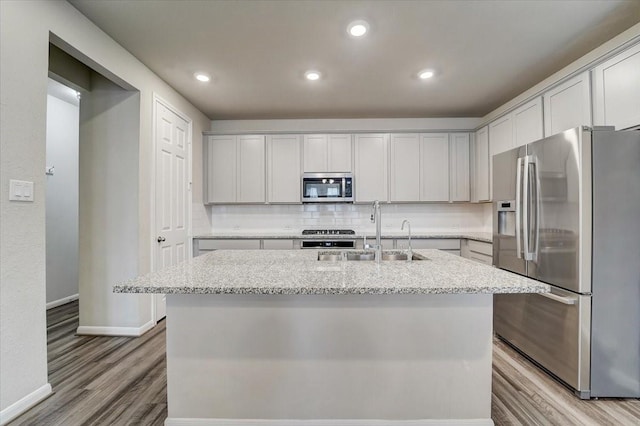 kitchen with stainless steel appliances, wood finished floors, a sink, and backsplash
