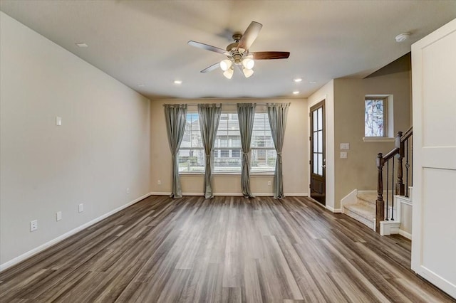 unfurnished living room featuring wood finished floors, a ceiling fan, baseboards, and stairway