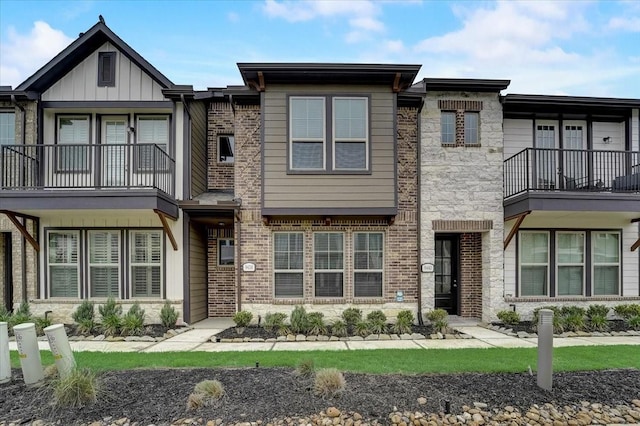 view of front of home featuring brick siding, stone siding, and a balcony