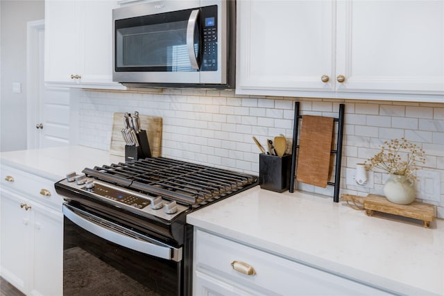 kitchen featuring white cabinets, decorative backsplash, light stone countertops, stainless steel microwave, and gas range