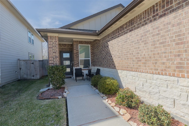 property entrance featuring fence, a lawn, board and batten siding, and brick siding