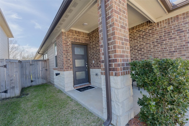 doorway to property with a yard, fence, and brick siding