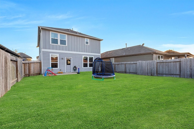 rear view of house featuring a trampoline, board and batten siding, a lawn, and a fenced backyard