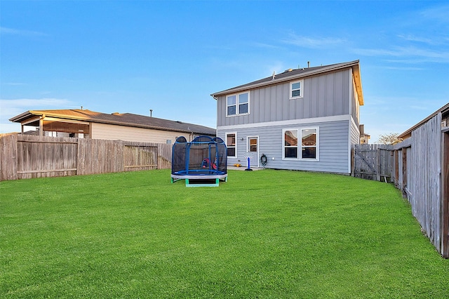 back of property with a fenced backyard, a trampoline, a lawn, and board and batten siding