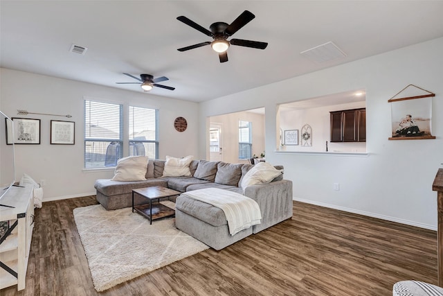 living room with dark wood-style floors, visible vents, baseboards, and a ceiling fan