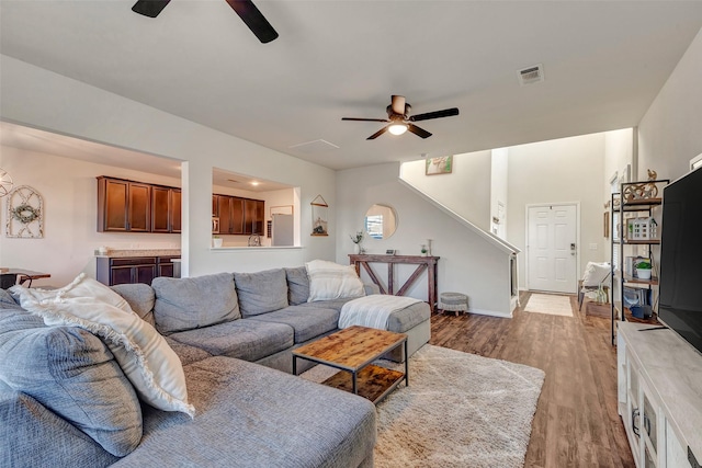 living area featuring baseboards, visible vents, ceiling fan, wood finished floors, and stairs