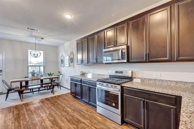 kitchen with light stone counters, stainless steel appliances, visible vents, light wood-style flooring, and dark brown cabinets