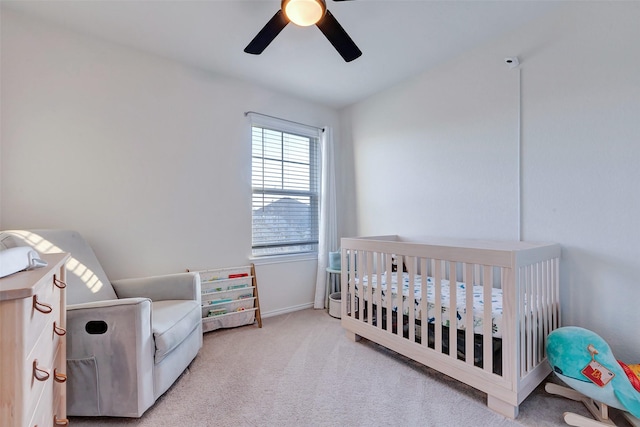 bedroom featuring light carpet, baseboards, a crib, and a ceiling fan