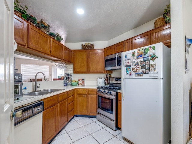 kitchen with brown cabinetry, appliances with stainless steel finishes, light countertops, a sink, and light tile patterned flooring