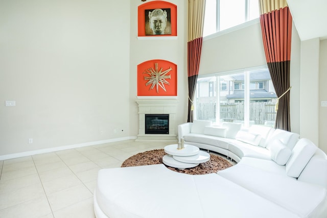 tiled living area featuring a high ceiling, a glass covered fireplace, and baseboards