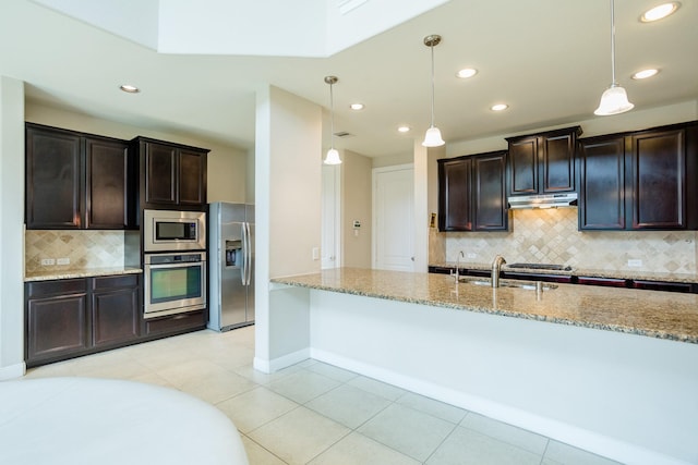 kitchen featuring under cabinet range hood, appliances with stainless steel finishes, light stone counters, and decorative light fixtures