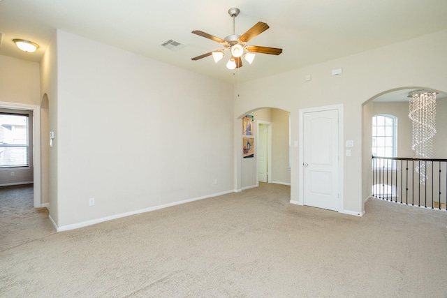 carpeted empty room with arched walkways, visible vents, ceiling fan, and baseboards