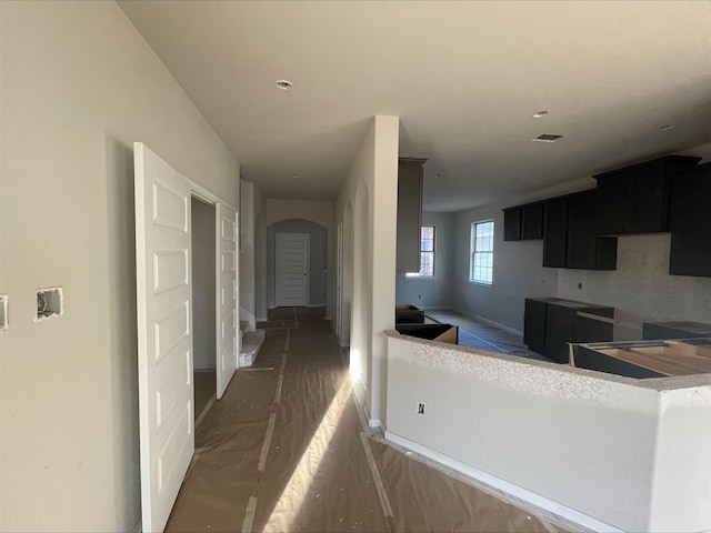 kitchen featuring arched walkways, dark cabinets, wood finished floors, visible vents, and baseboards