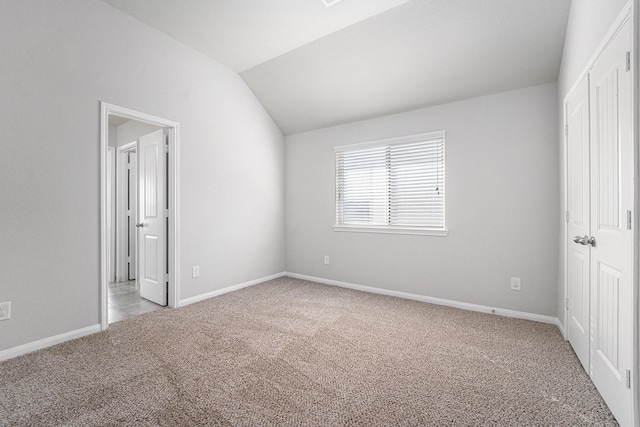 unfurnished bedroom with lofted ceiling, a closet, baseboards, and light colored carpet