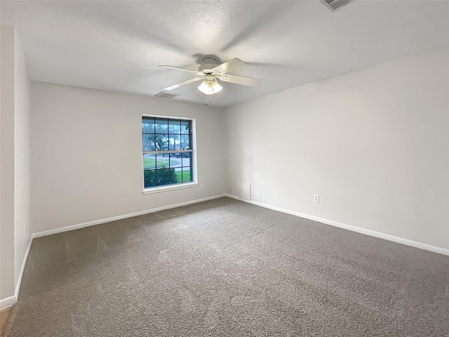 spare room with baseboards, visible vents, dark carpet, and a ceiling fan