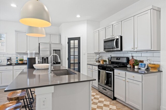 kitchen with a sink, a kitchen breakfast bar, backsplash, dark countertops, and appliances with stainless steel finishes