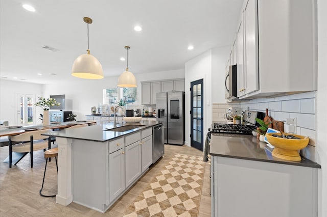 kitchen featuring visible vents, a sink, appliances with stainless steel finishes, dark countertops, and tasteful backsplash