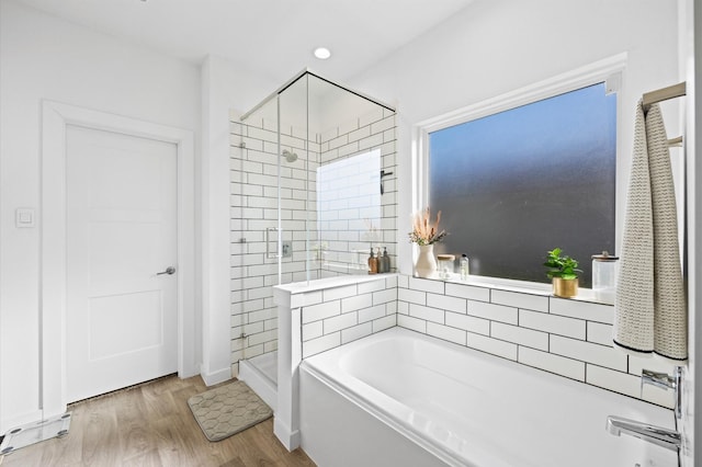 full bathroom featuring a bath, a shower stall, and wood finished floors