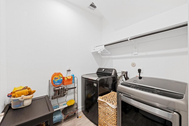 clothes washing area featuring washing machine and clothes dryer, laundry area, light wood-type flooring, and visible vents