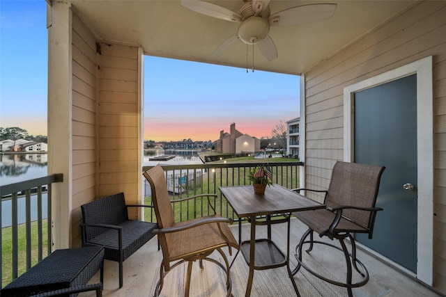 balcony at dusk with a water view and ceiling fan